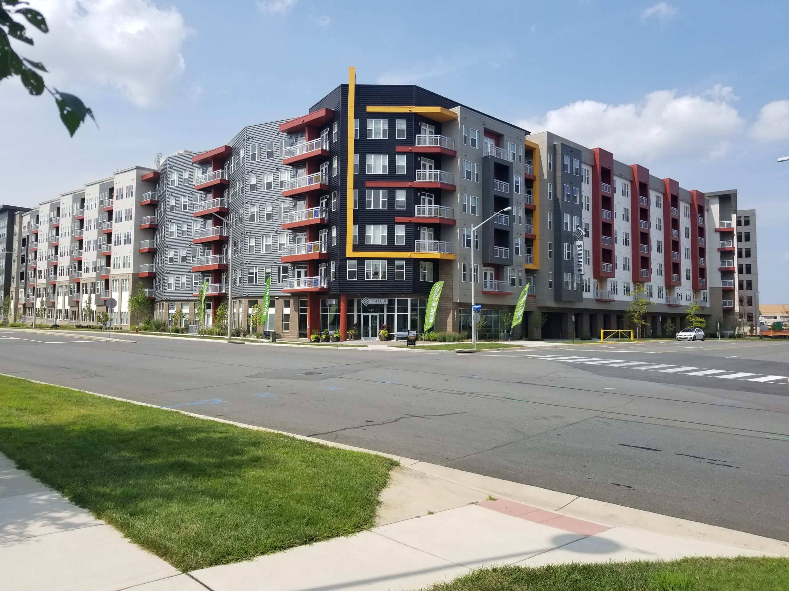 Exterior view of Dulles Station multi-family residential building in Herndon, VA, featuring a 4-story wood-frame structure with modern colorful facade accents and ground-level storefronts.