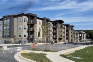 The Overlook at Franklin Square: Exterior Development Exterior view of a modern multi-family apartment complex featuring stone veneer and siding finishes, currently under late-stage construction with paved parking areas in the foreground.