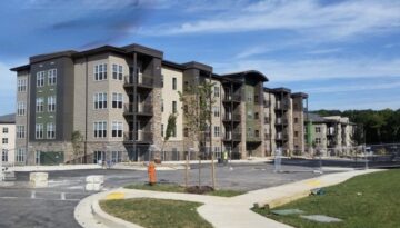 Exterior view of a modern multi-family apartment complex featuring stone veneer and siding finishes, currently under late-stage construction with paved parking areas in the foreground.