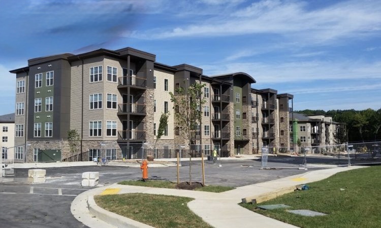 Exterior view of a modern multi-family apartment complex featuring stone veneer and siding finishes, currently under late-stage construction with paved parking areas in the foreground.